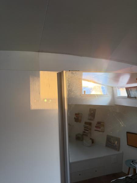 Golden sunlight streams into a cozy houseboat interior, reflecting off a large mirror and illuminating a bed with storage